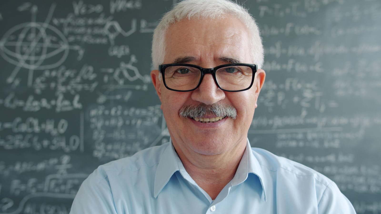 Docente sonriente frente a un tablero en su salón de clase.